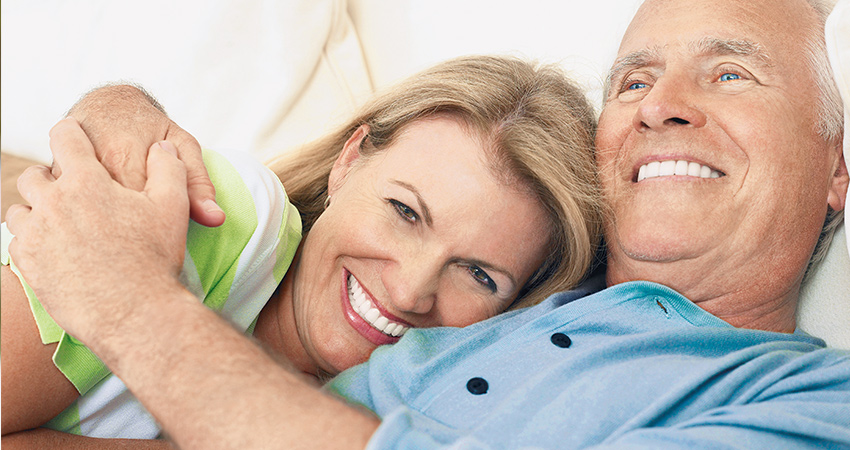 Retired couple with dental implants embraces in bed
